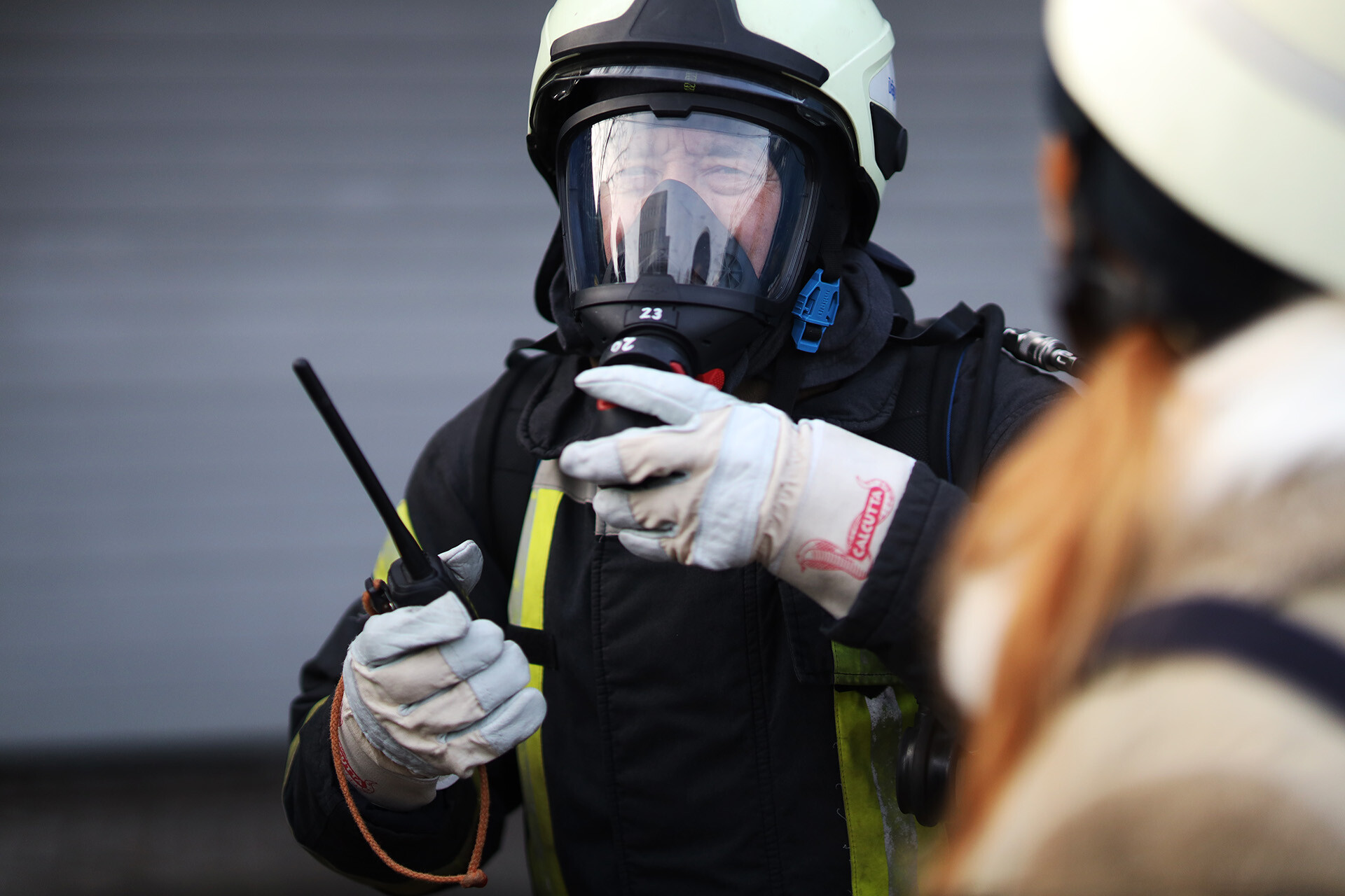 Person in Feuerwehrkleidung mit Walkie Talkie in der Hand. 