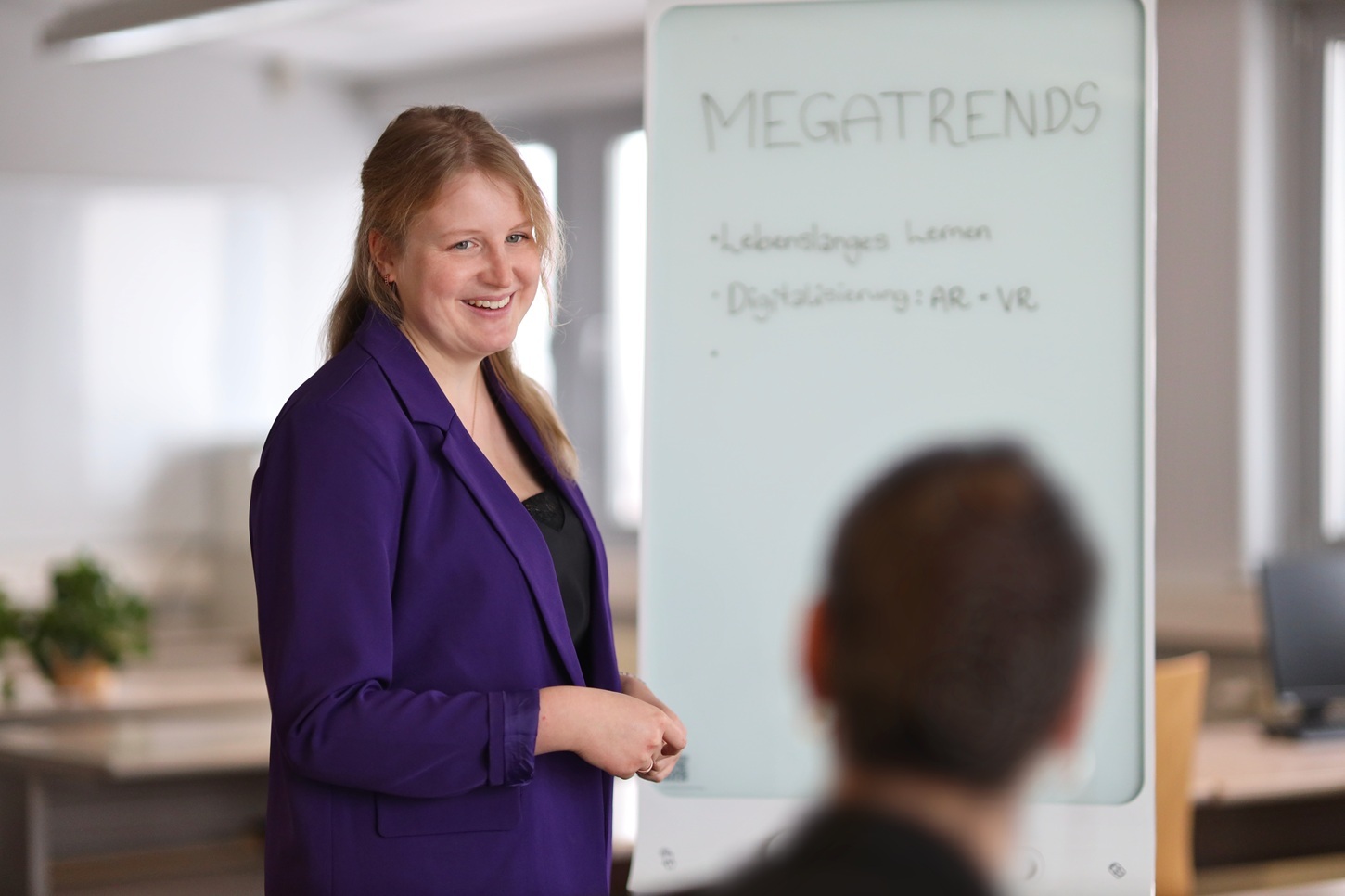 Frau vor einem Flipchart blickt lächelnd zu einem Teilnehmer